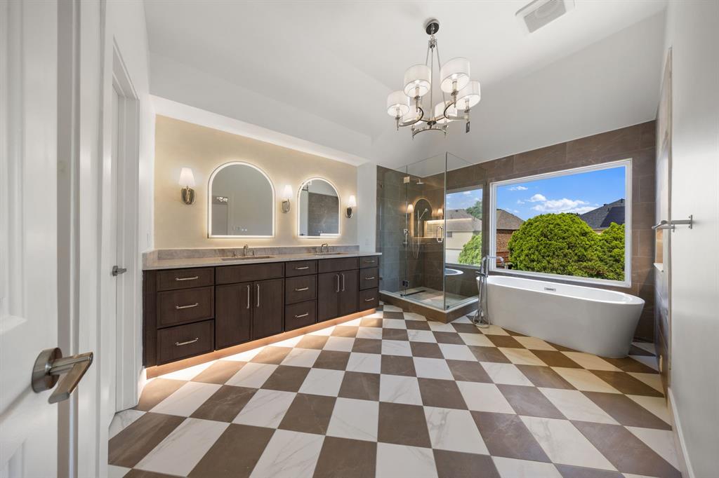 Spacious bathroom featuring checkered tile flooring, a freestanding soaking tub, a frameless glass shower enclosure, a dual vanity with undermount sinks, and illuminated arched mirrors Spacious bathroom featuring checkered tile flooring, a freestanding soaking tub, a frameless glass shower enclosure, a dual vanity with undermount sinks, and illuminated arched mirrors