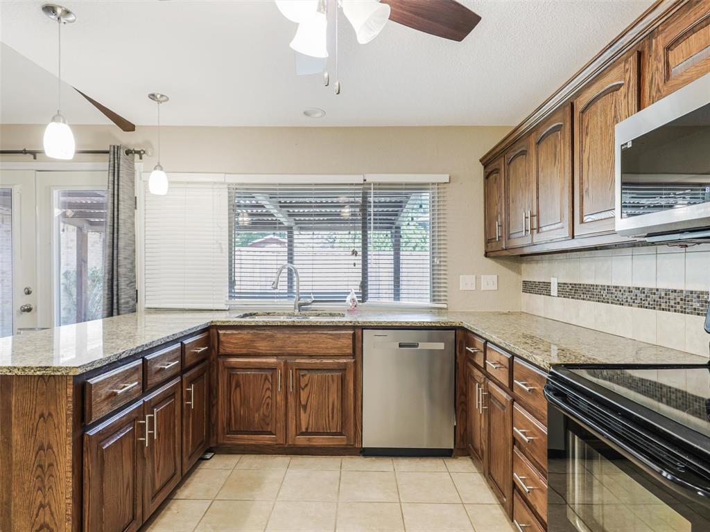 Kitchen featuring wood cabinetry, granite countertops, tile flooring, stainless steel dishwasher, and pendant lighting