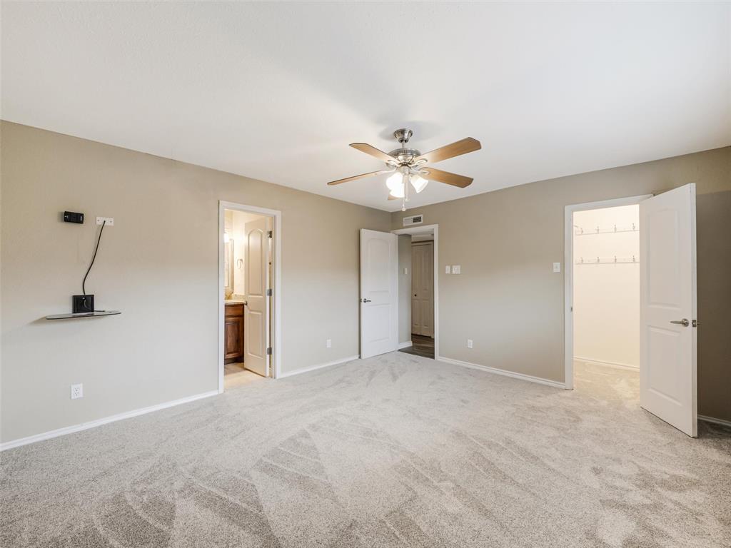 Spacious room with light neutral wall tones, gray patterned carpet, ceiling fan with integrated lighting, and multiple white panel doors