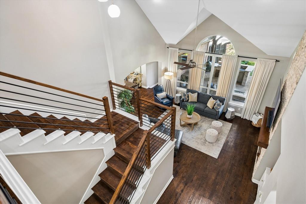 Vaulted ceilings with an arched window, wood-finish flooring, staircase with metal spindles, and a ceiling fan
