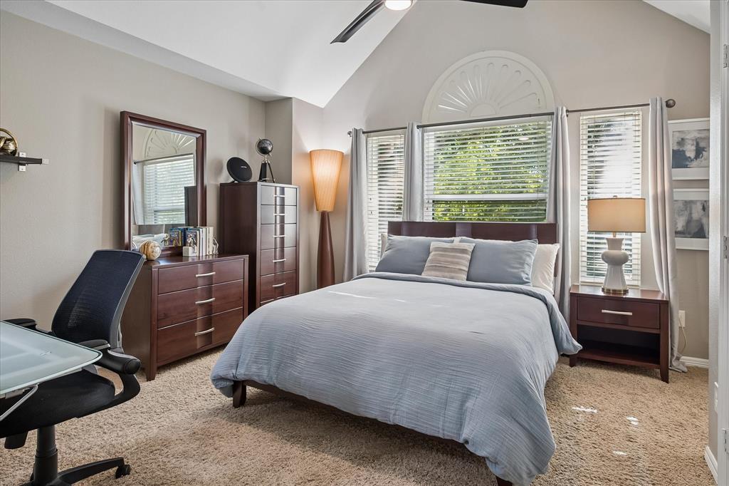 Vaulted ceiling with an overhead fan, arched window with decorative trim, multiple windows with blinds, and carpet flooring