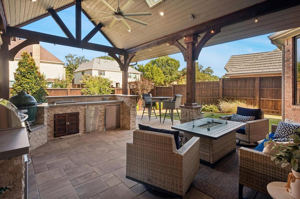 Covered patio featuring a slatted ceiling, exposed wood beams, a built-in outdoor kitchen with stone veneer, and paver flooring