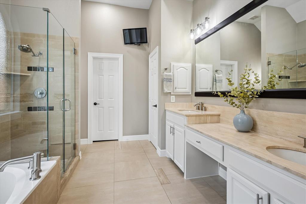 Spacious bathroom featuring a double vanity with stone countertops, white cabinetry, a large frameless glass shower enclosure, and a built-in bathtub