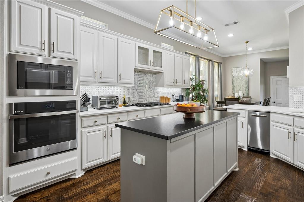 White cabinetry with brushed nickel hardware, stainless steel appliances, dark wood-finish flooring, a kitchen island with a dark countertop, and a tiled backsplash