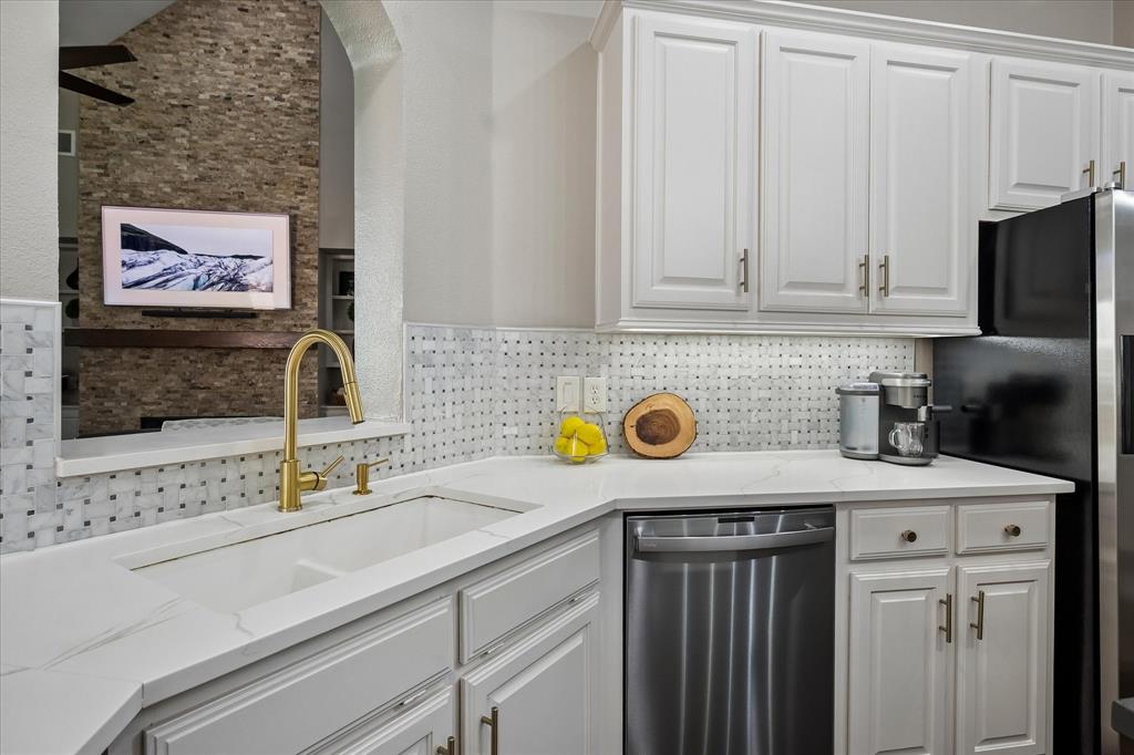 White cabinetry with gold-tone hardware, white countertop surfaces, and a mosaic tile backsplash