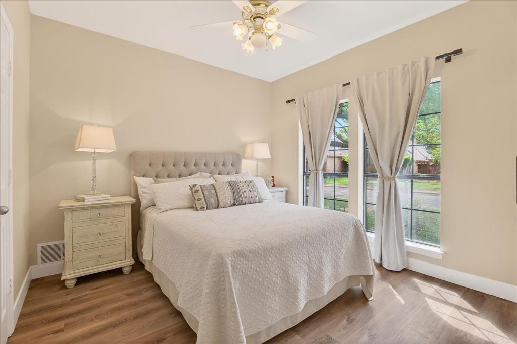 Wood-finish flooring, tufted upholstered headboard, dual windows, and ceiling fan with integrated lighting