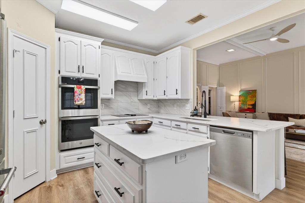 White cabinetry with black hardware, double wall ovens, wood-finish flooring, white countertops, and a built-in dishwasher
