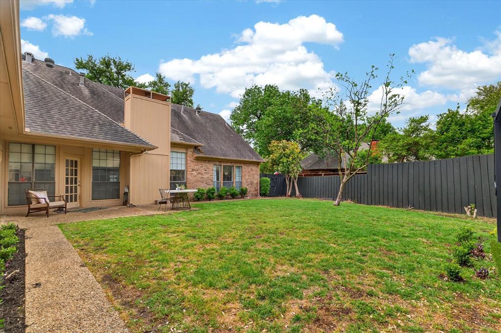 Expansive backyard with a manicured lawn, brick exterior, dedicated patio area, and a mature tree
