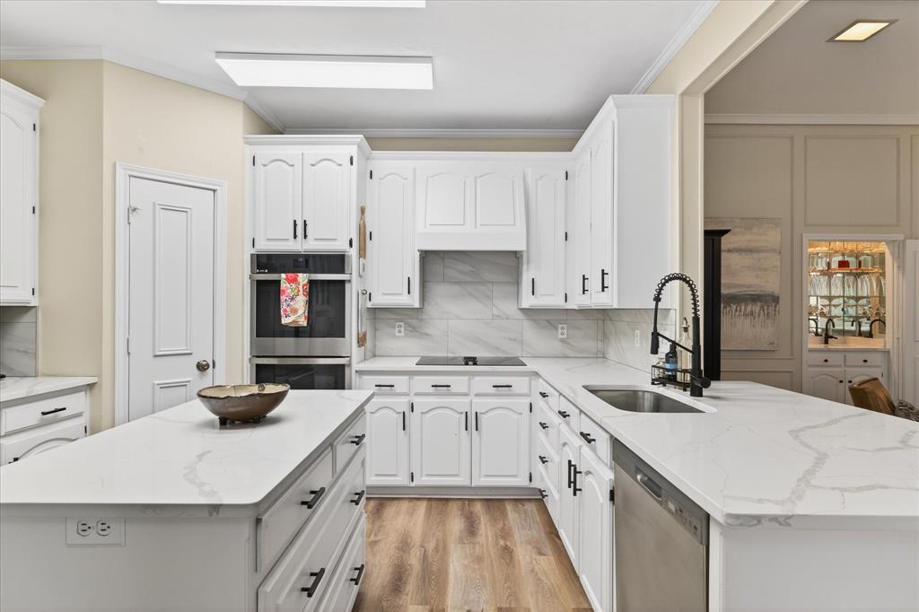 White cabinetry with black hardware, stainless steel appliances, wood-finish flooring, white countertops, and a white tile backsplash
