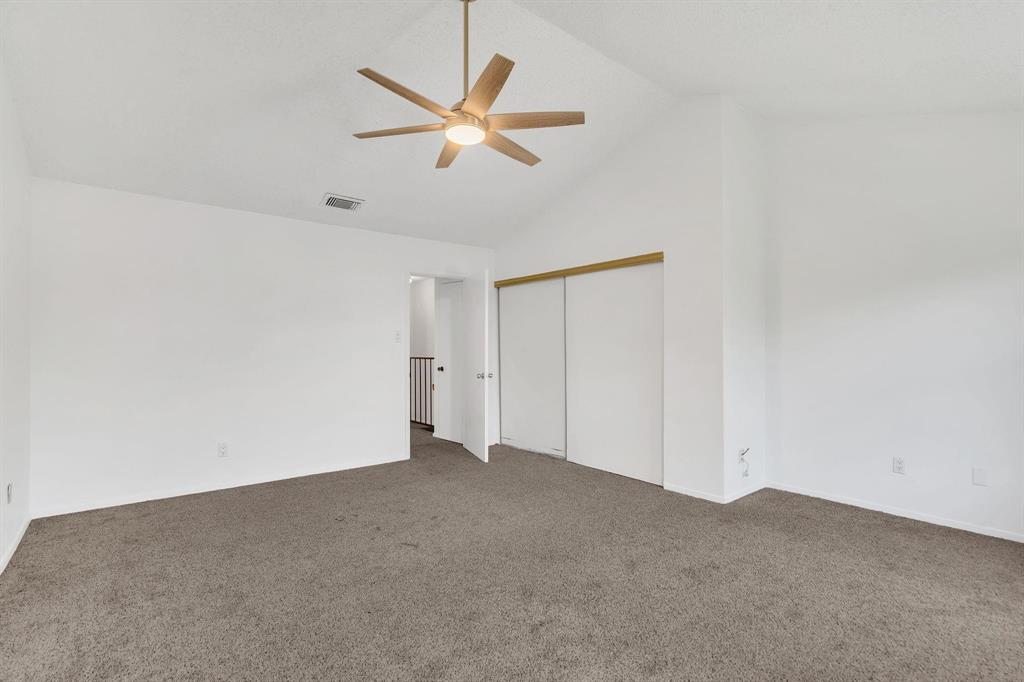 Vaulted ceiling, ceiling fan with integrated lighting, carpeted flooring, sliding closet doors, and neutral wall tones