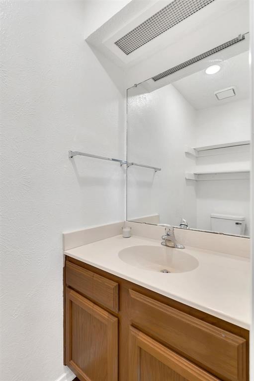 Vanity with wood-finish cabinetry, integrated sink, and light-toned countertop