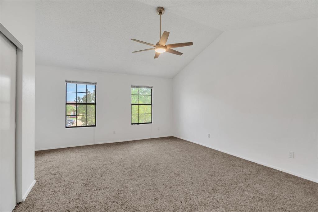 Vaulted ceiling with a ceiling fan and integrated lighting, two double-hung windows, wall-to-wall carpeting, and a built-in closet with sliding doors