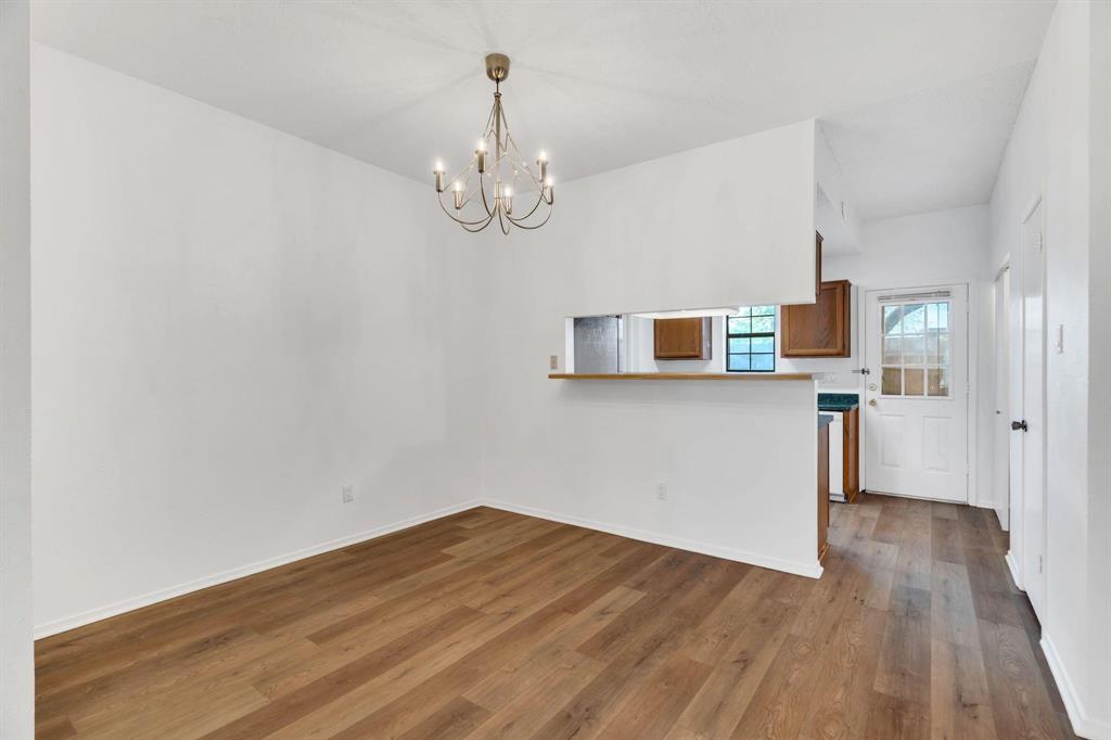 Wood-finish flooring, overhead chandelier, white walls, passthrough counter, and a paneled door