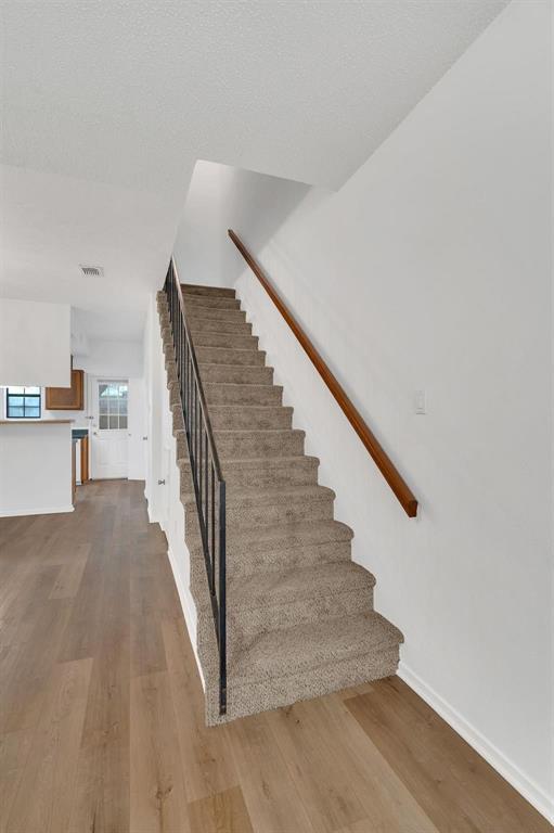 Carpeted staircase with a wood handrail, black metal balusters, and wood-finish flooring