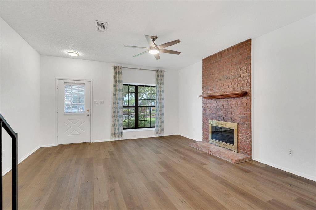 Wood-finish flooring throughout, brick fireplace with a wood mantel, ceiling fan, and a transom-style door