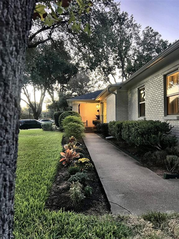Brick exterior with multiple windows, concrete walkway, landscaped garden bed, and mature trees
