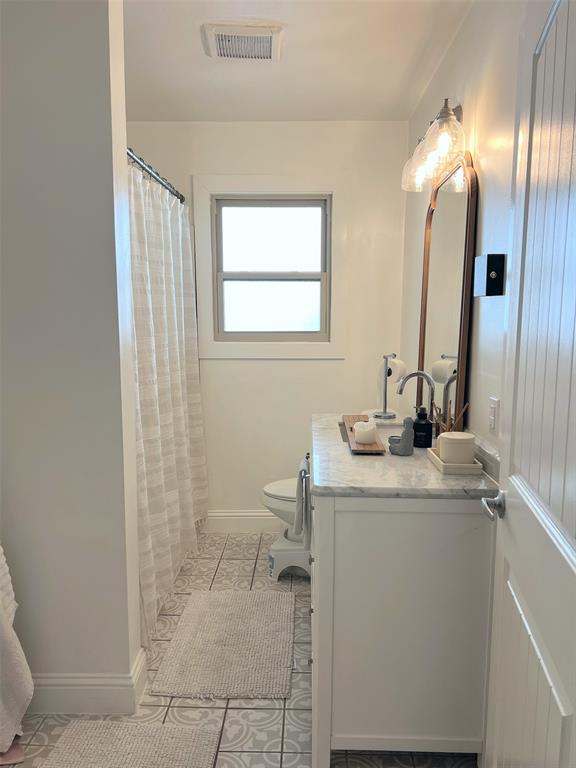 White single vanity with a marble-finish countertop, patterned floor tiling, and a window