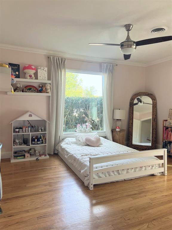 Hardwood flooring, large window with drapes, crown molding, and a ceiling fan with integrated lighting