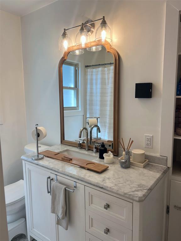 White vanity with shaker-style cabinetry, a stone countertop, and a single basin undermount sink