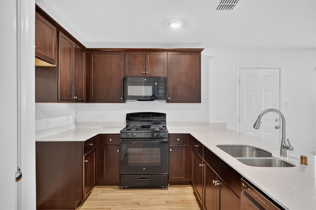 U-shaped kitchen featuring dark wood cabinetry, light-colored countertops, a black range with an oven, a built-in microwave, and wood-finish flooring