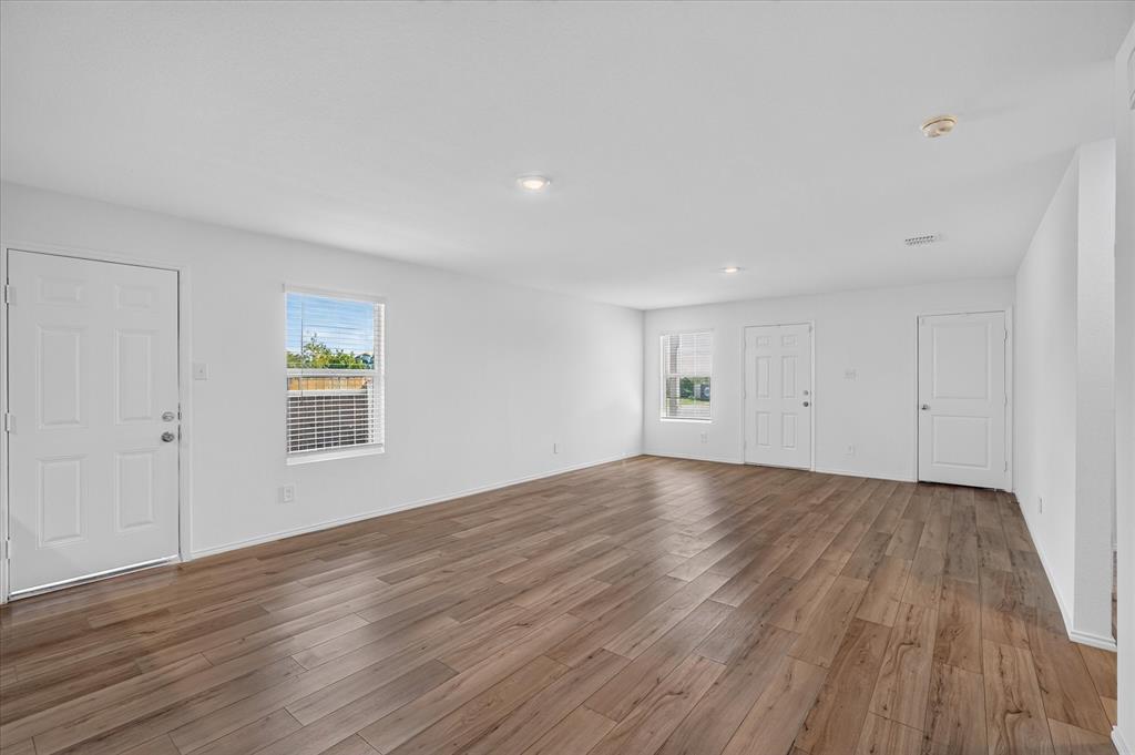 Spacious room featuring wood-finish flooring, multiple windows with blinds, recessed lighting, and white paneled doors