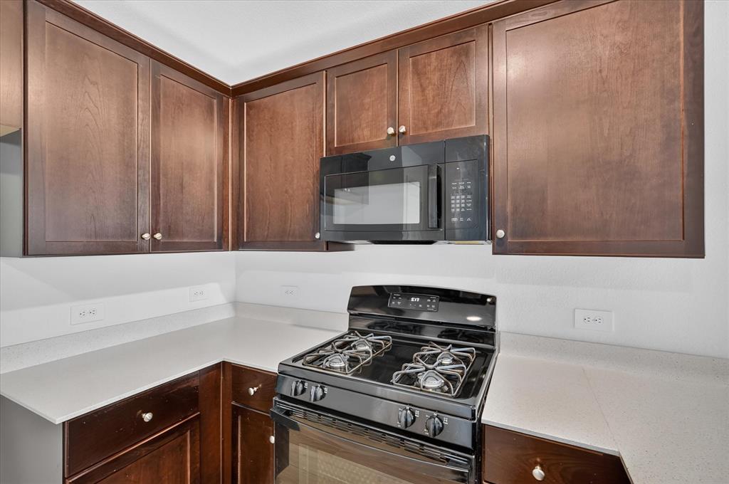 Rich wood cabinetry, light-toned countertops, a built-in microwave, and a black range