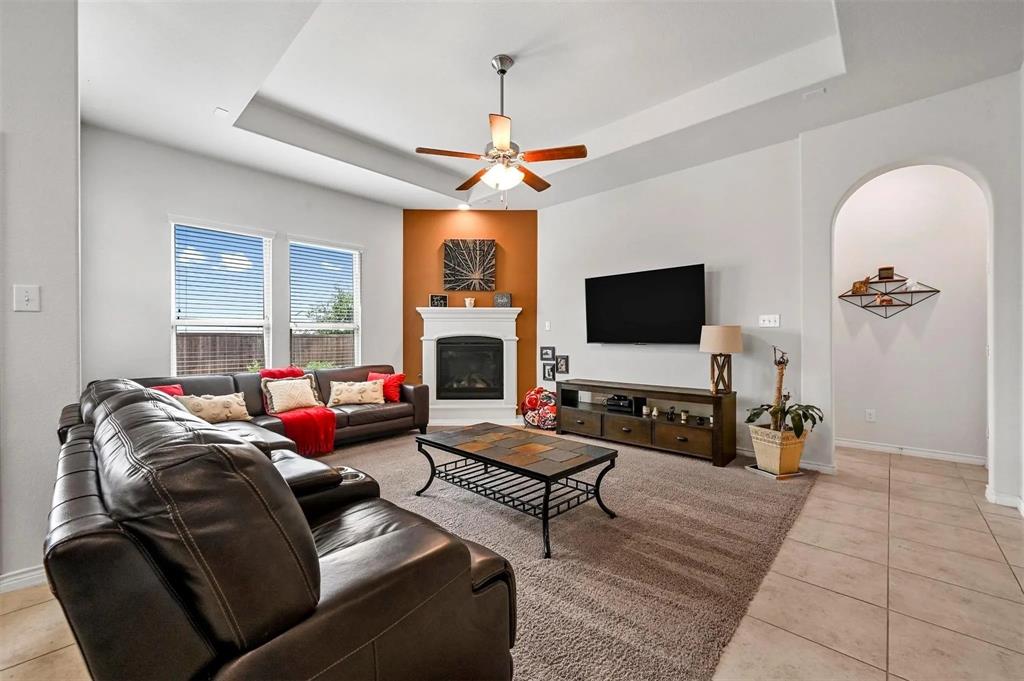Living area featuring a tray ceiling, ceiling fan, and a built-in fireplace with white mantel Living area featuring a tray ceiling, ceiling fan, and a built-in fireplace with white mantel