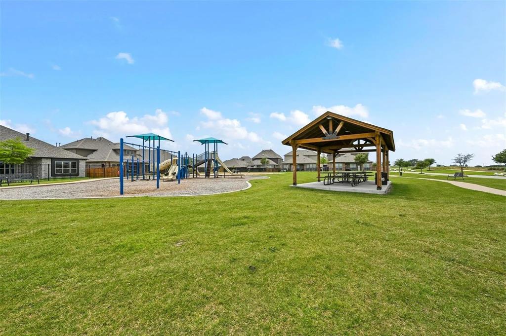 Expansive green space featuring a playground structure, a covered picnic area, and paved walking paths