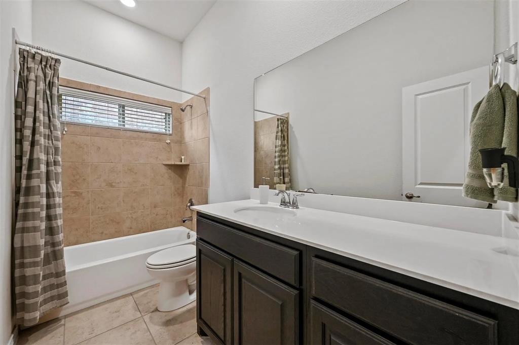 Bathroom featuring a built-in tub with tile surround, a dark wood-finish vanity with an integrated sink, a large wall-mounted mirror, and tiled flooring