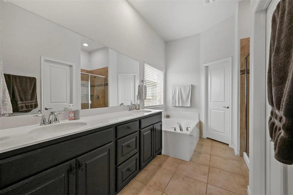 Dual vanity with undermount sinks, built-in bathtub, separate glass-enclosed shower, expansive wall mirror, and tile flooring