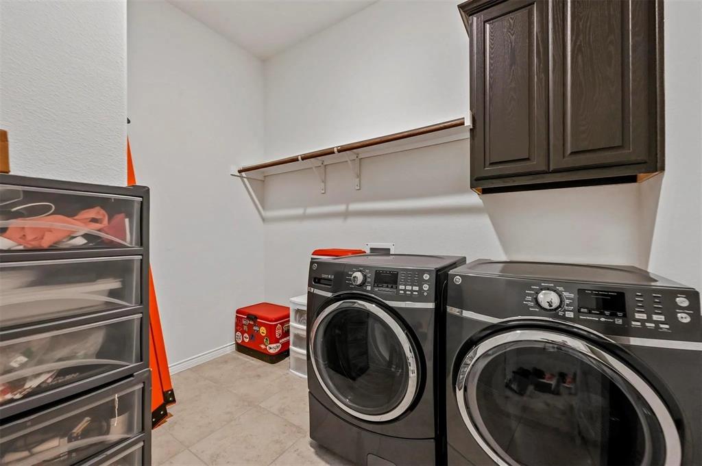 Laundry area featuring tile flooring, a built-in wall cabinet, and a wall-mounted shelving unit with a hanging rod