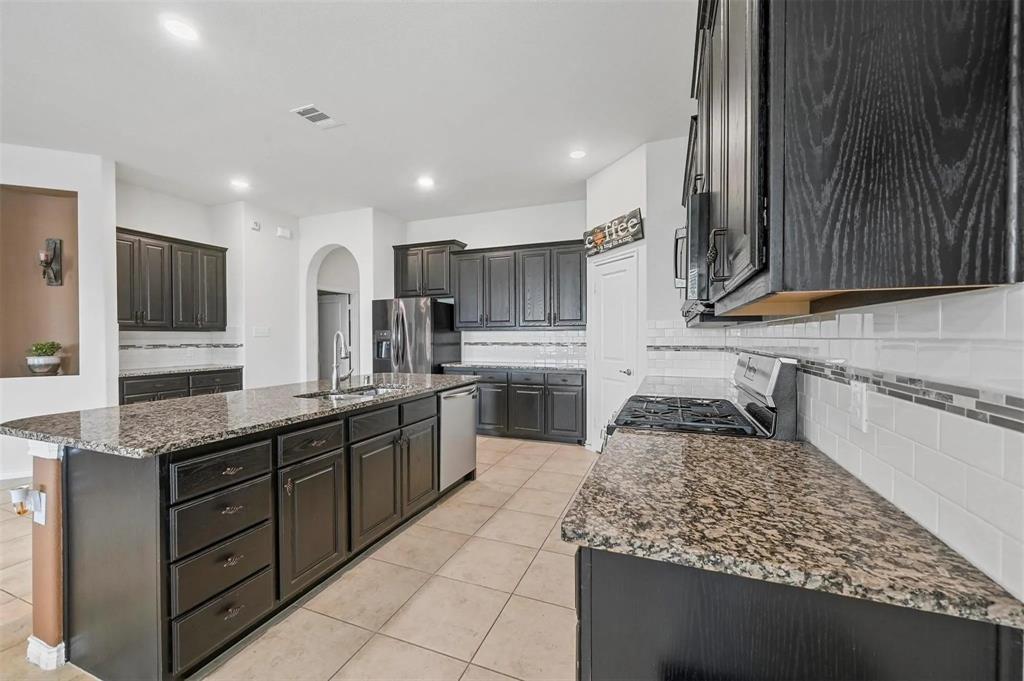 Kitchen featuring dark wood-finish cabinetry, granite countertops, tile flooring, stainless steel appliances, and an expansive center island with an undermount sink