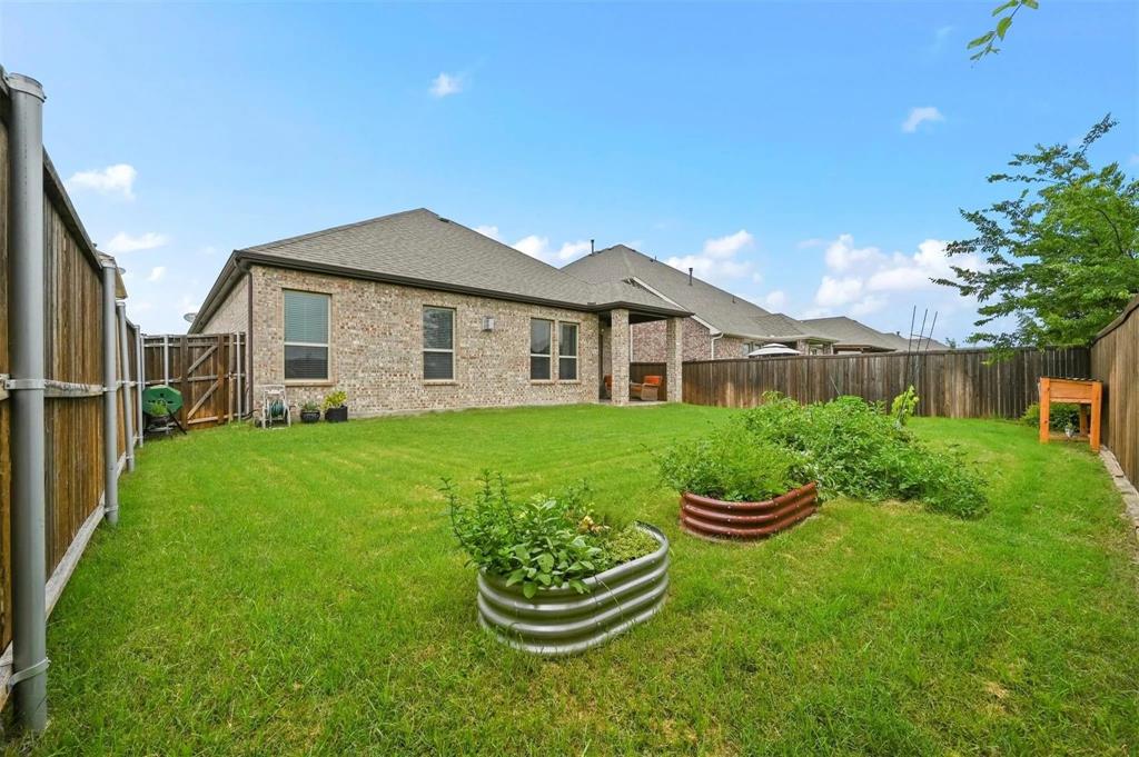 Expansive backyard featuring a manicured lawn, full privacy fencing, and raised garden beds