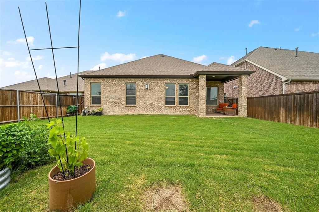 Expansive backyard with a manicured lawn, full brick exterior, covered patio, and privacy fencing