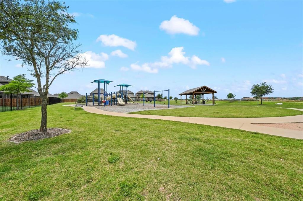 Expansive green space featuring a playground with shade structures, a covered picnic area, and paved walking paths