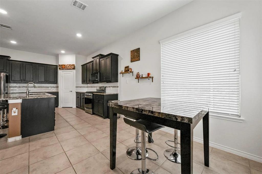 Kitchen featuring dark wood cabinetry, stainless steel appliances, a tile backsplash, and stone-finish countertops Kitchen featuring dark wood cabinetry, stainless steel appliances, a tile backsplash, and stone-finish countertops