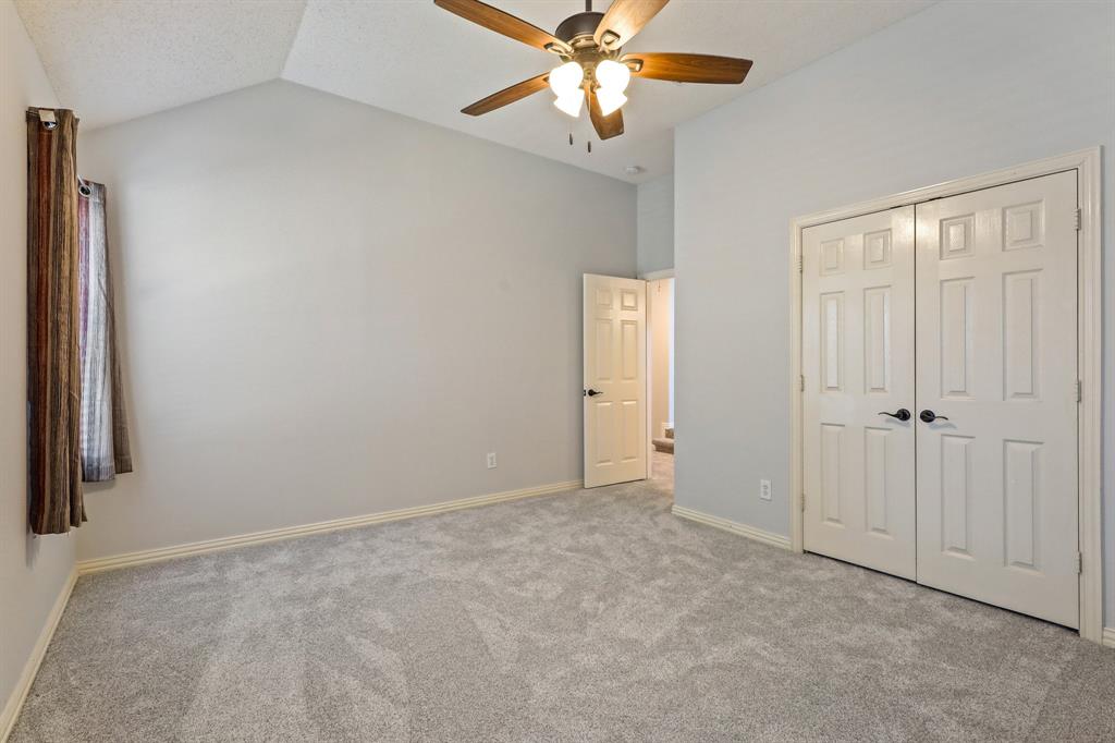 Vaulted ceiling with a centrally mounted ceiling fan, neutral carpeting, and dual-panel closet doors