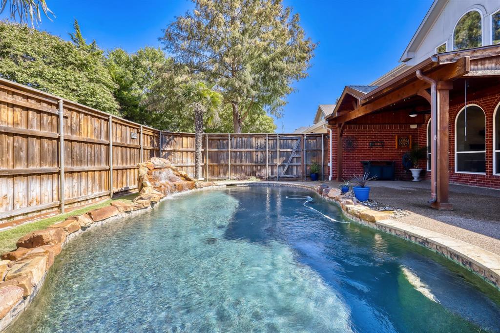 Backyard pool featuring a rock-lined water feature, stone coping, and a covered patio with a wooden beam structure and red brick exterior