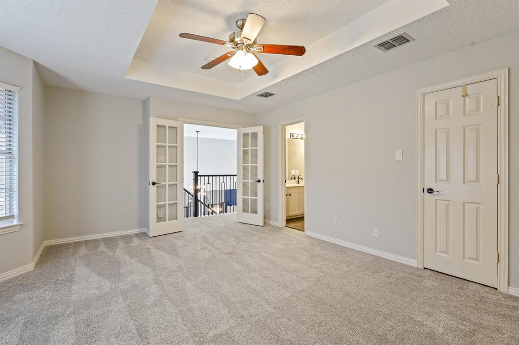 Tray ceiling featuring a central lighted ceiling fan, complemented by French doors, neutral carpeting, and a multi-panel door