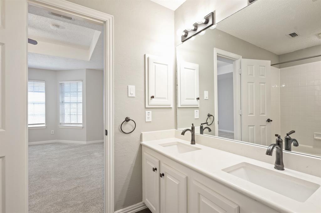 Dual-sink vanity with white cabinetry, solid surface countertop, oil-rubbed bronze faucets, and full-width vanity mirror