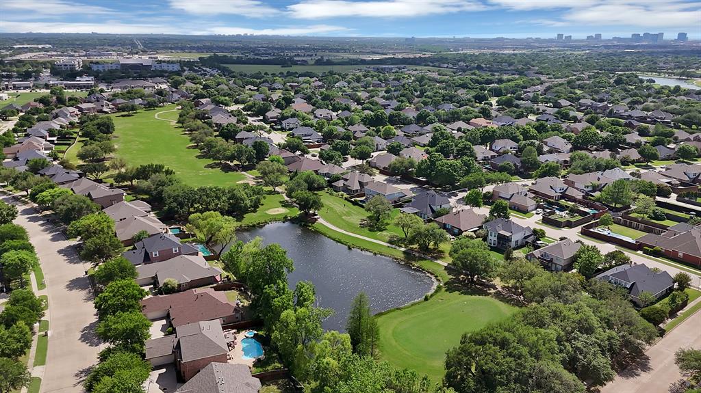 Aerial perspective featuring a natural pond, surrounding green space, mature trees, and established neighborhood infrastructure