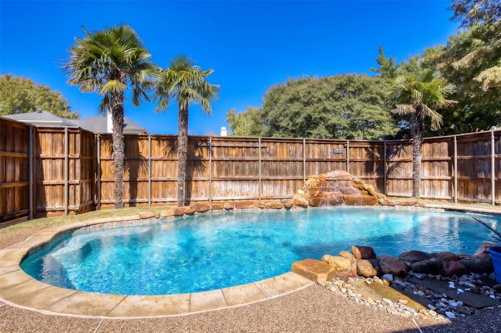 In-ground swimming pool featuring a rock waterfall, flagstone-style coping, and privacy wood fencing