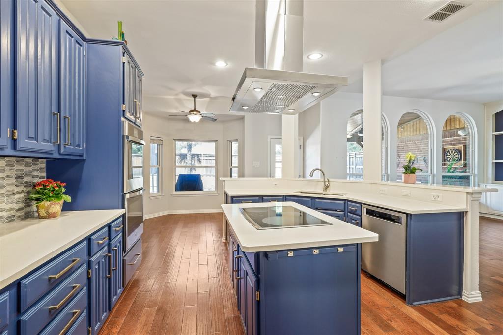 Kitchen featuring blue cabinetry, a central island with a built-in cooktop, stainless steel range hood, wood-finish flooring, and arched windows