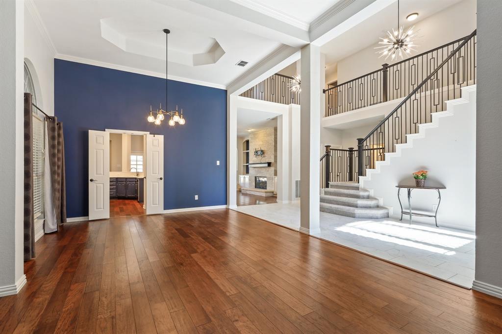 Foyer and living area featuring wood-finish flooring, a double-height ceiling with a tray architectural detail, an iron-railed staircase, and dual statement chandeliers