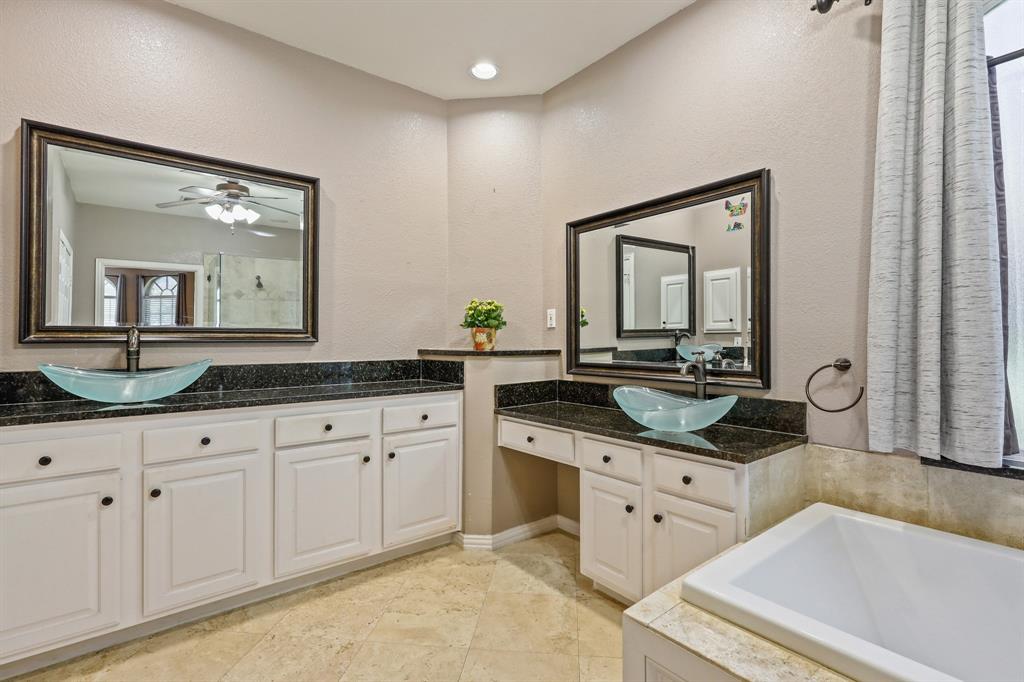 Dual vanity featuring white cabinetry, dark stone countertops, glass vessel sinks, framed mirrors, and tile flooring