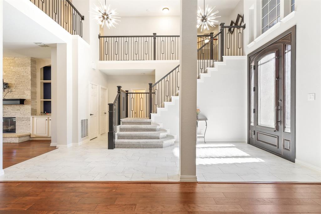 Grand foyer featuring a two-story ceiling, stone tile flooring, a staircase with decorative metal railings, dual starburst pendant light fixtures, and a glass-paneled entry door