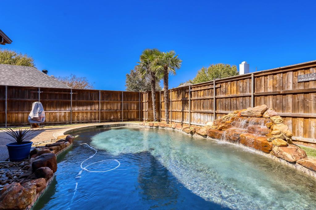 Private outdoor space featuring a freeform swimming pool, stone waterfall feature, aggregate pool deck, and full-height wood privacy fencing