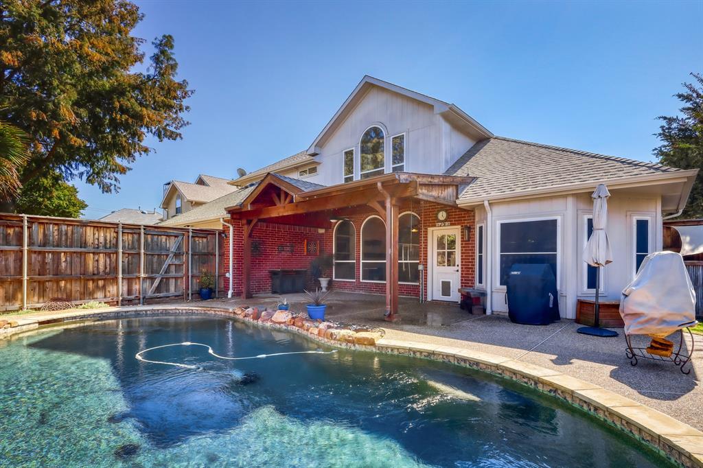 In-ground swimming pool with stone coping, covered patio with wood-beam framing, brick and siding exterior, and wood privacy fencing