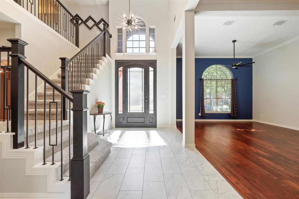 Grand foyer featuring stone-look tile flooring, an arched glass-paneled entry door, a starburst chandelier, and a staircase with decorative wrought iron railings