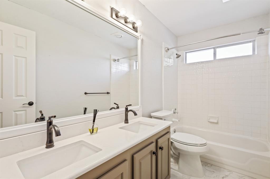 Dual-sink vanity with quartz countertop, under-mount basins, dark finish fixtures, and full-width vanity mirror, complemented by a white tiled tub-shower combination